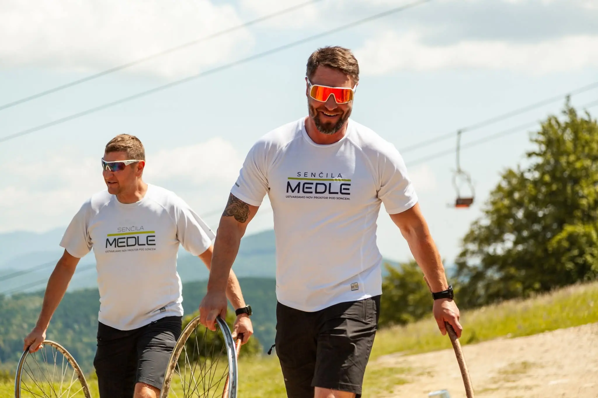 Dva moška v športnih oblačilih, ki nosita obroče na prostem s kabinsko žičnico v ozadju.