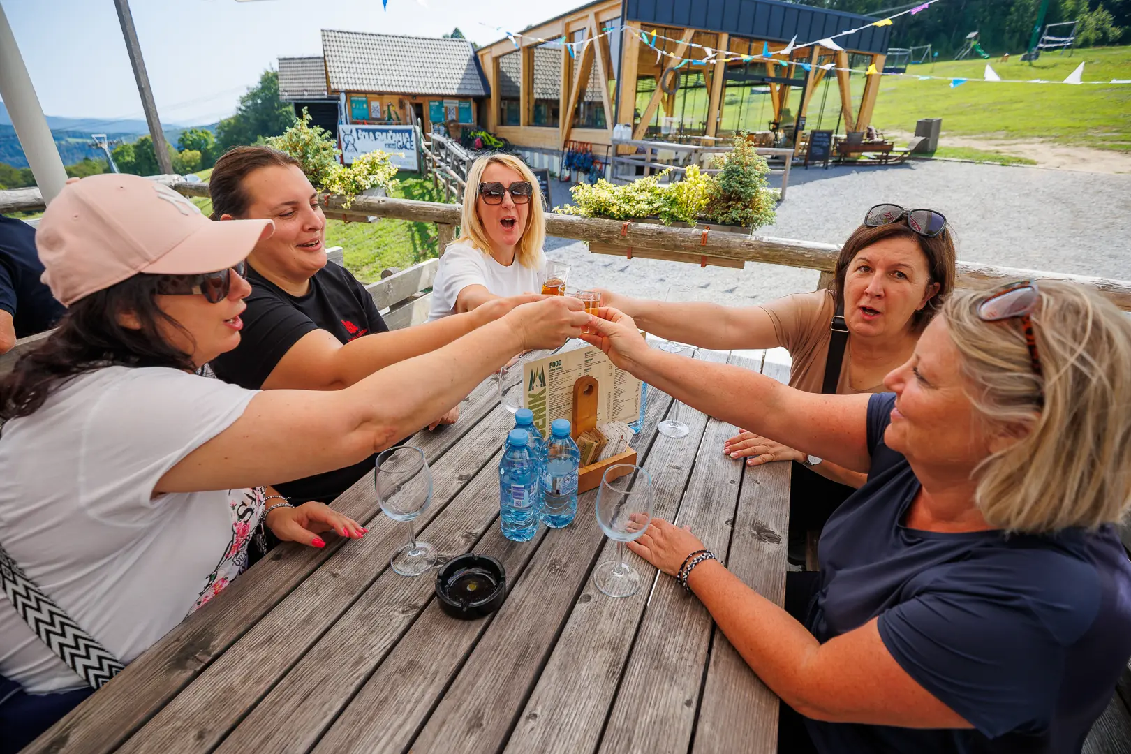 Skupina žensk na terasi dviguje kozarce v pozdrav.