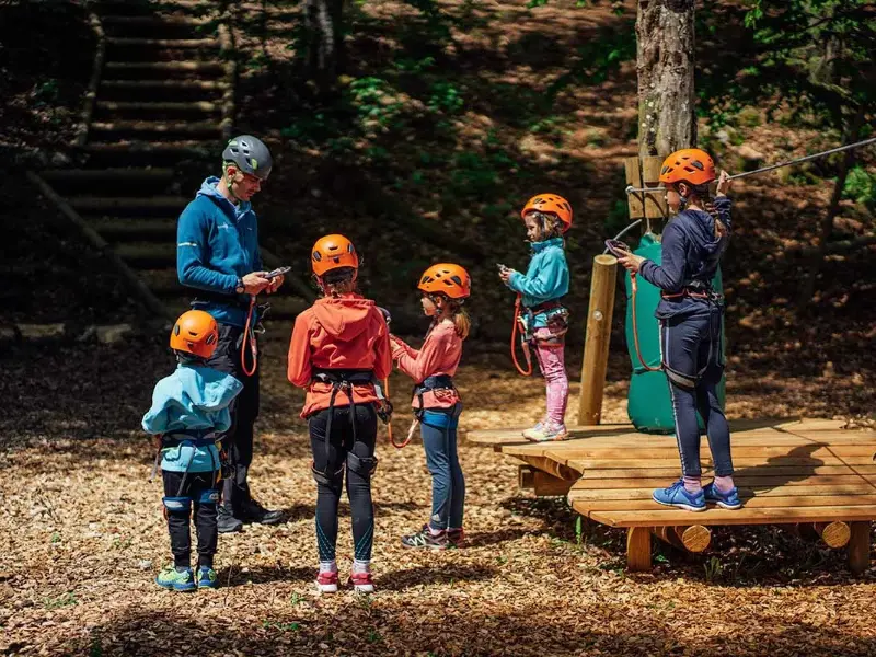 Skupina otrok v čeladah se pripravlja na zipline v gozdnem okolju.