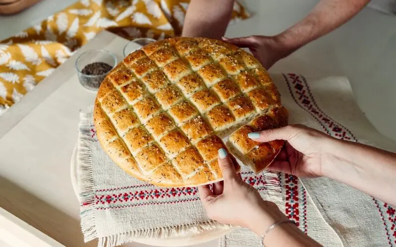 People holding freshly baked homemade bread on a decorative cloth