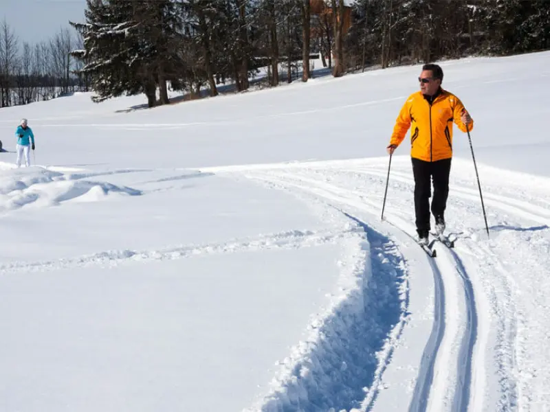 Moški v oranžni jakni smuča po zasneženi poti